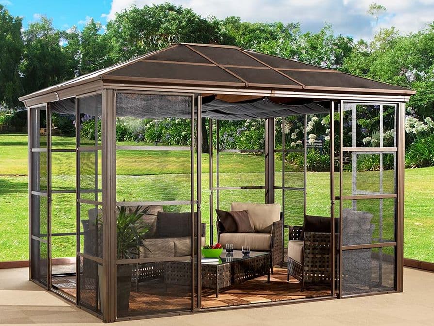 Moderner Gartenpavillon mit Glas- und Aluminiumrahmen, ausgestattet mit bequemen Polstermöbeln und einem gedeckten Dach in einem grünen Garten.