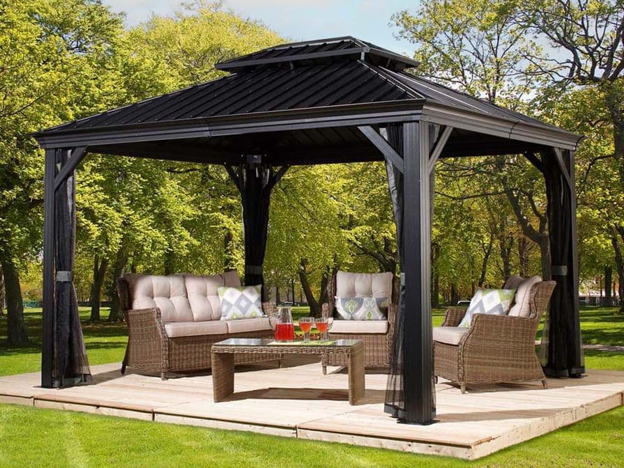 Freistehender, schwarzer Gartenpavillon mit robustem Dach und gemütlicher Polstermöbelgruppe auf einer Holzterrasse in einem grünen Garten.