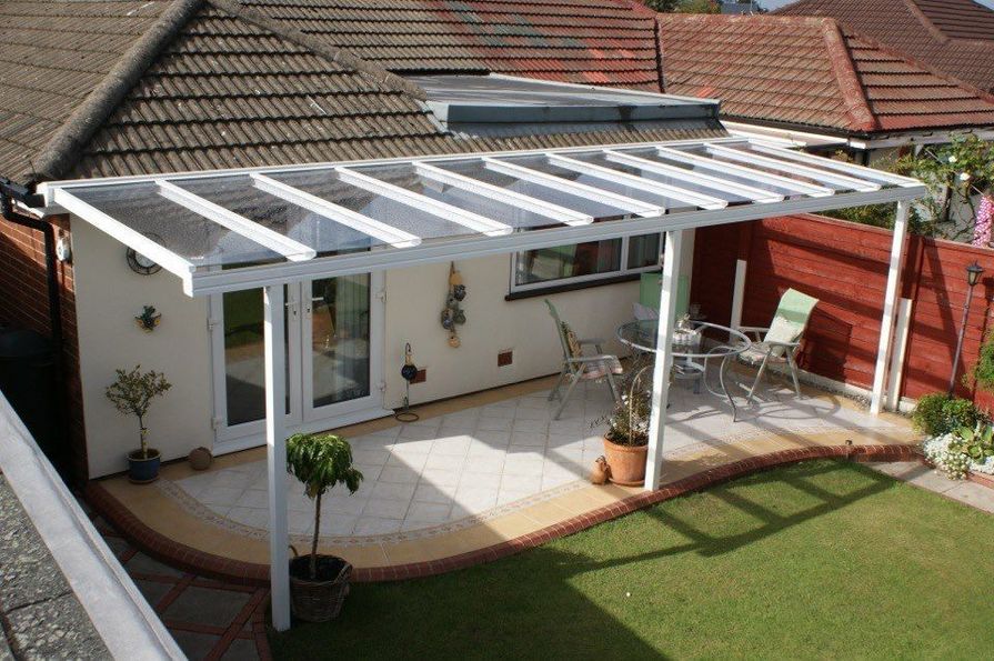 Elegante weiße Wandergola mit Glasdach an einem Haus über einer gefliesten Terrasse mit Terrassenmöbeln